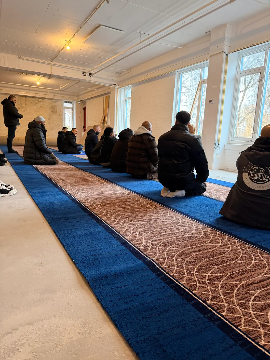 Rijen biddende mannen op het blauwe gebedstapijt, van achteren gezien