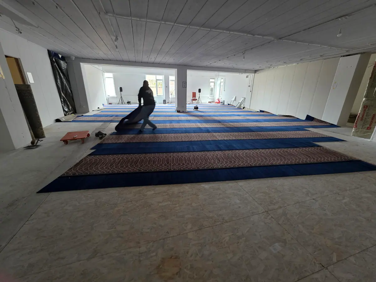 Een vrijwilliger rolt een baan gebedstapijt uit in de zaal